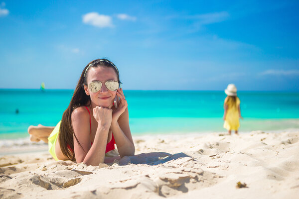 Молодая женщина лежит на белом песке и разговаривает по телефону
