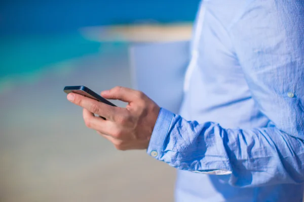 Close-up van telefoon in mannenhand op tropisch strand — Stockfoto