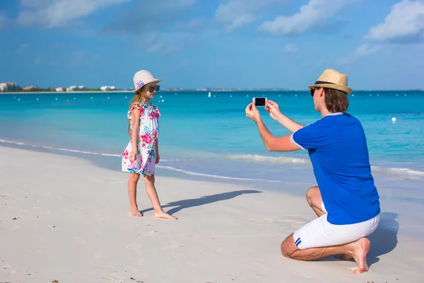 Молодой отец делает фото по телефону маленькой девочки на пляже — стоковое фото