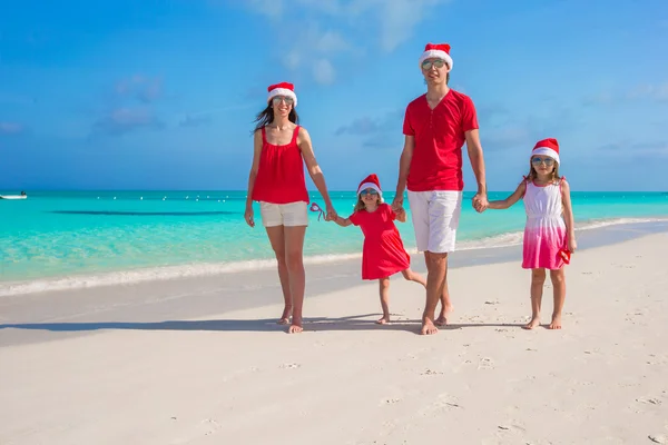 Happy family of four on beach in red Santa hats — Stock Photo, Image