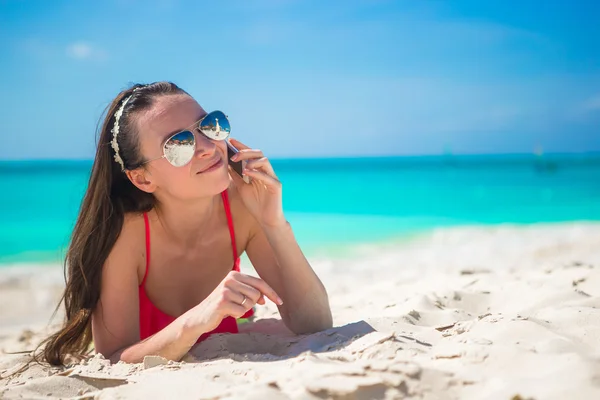 Young woman lying on white sand and talking by her phone — Stock Photo, Image