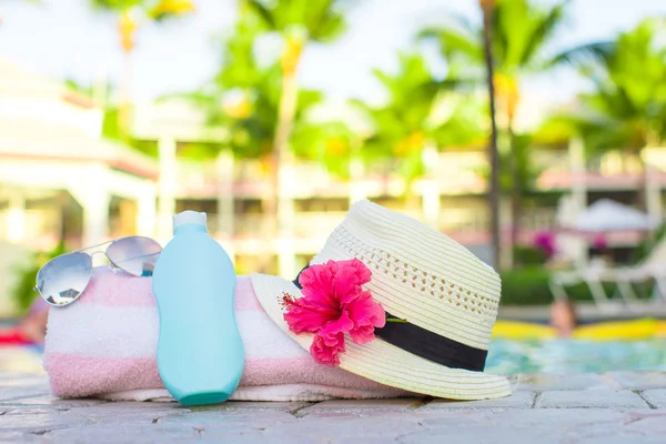 Crema solar, sombrero, gafas de sol, flores y torre cerca de la piscina — Foto de Stock