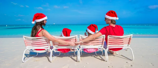 Vista trasera de la familia en sombreros de Navidad divirtiéndose en la playa tropical —  Fotos de Stock