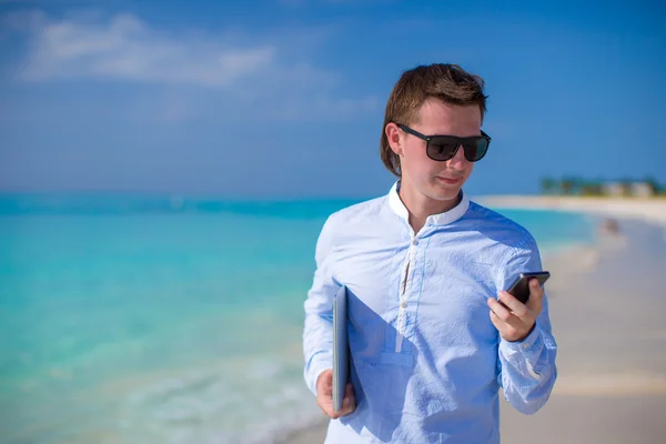 Młody biznesmen za pomocą laptopa i telefon na tropikalnej plaży — Zdjęcie stockowe