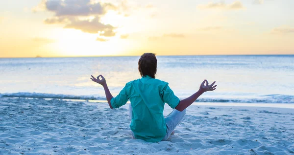 Young man sitting in lotus position on white sand beach — Stock Photo, Image