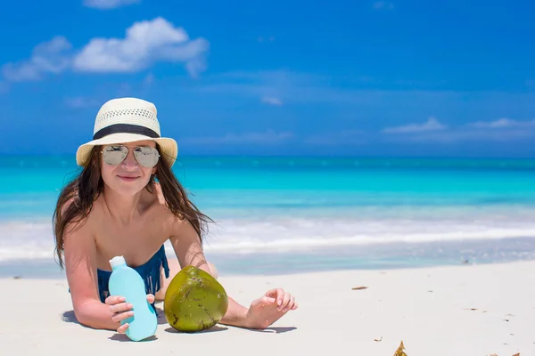 Beautiful young woman holding a suncream lying on tropical beach — Stock Photo, Image