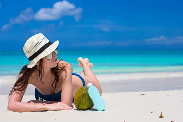 Hermosa joven sosteniendo una crema solar acostada en la playa tropical — Foto de Stock
