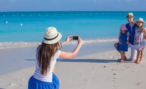 Joven madre haciendo foto en el teléfono de su familia en la playa — Foto de Stock