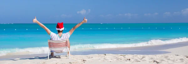 Vista trasera del joven en sombrero de Navidad en la silla de playa —  Fotos de Stock