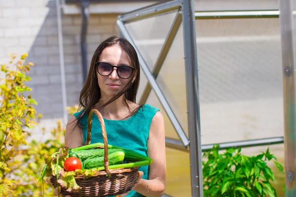 Mladá žena drží košík zeleně a cibule ve skleníku — Stock fotografie