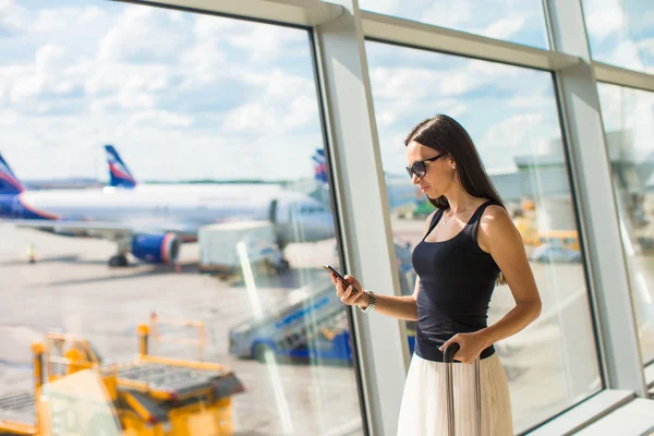 Mujer joven escribiendo un mensaje en el teléfono mientras espera el vuelo —  Fotos de Stock