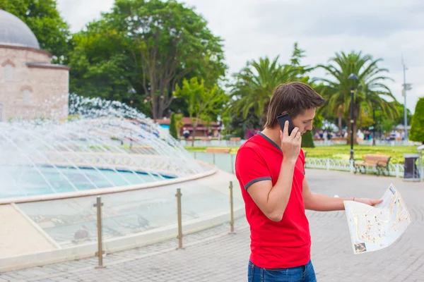 Młody człowiek przy użyciu telefonu z mapą w ręce — Zdjęcie stockowe