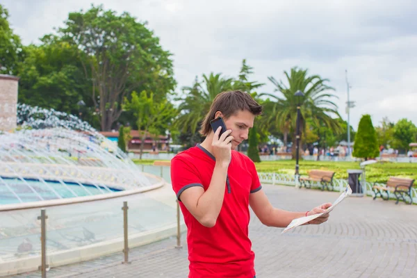 Młody człowiek przy użyciu telefonu z mapą w ręce — Zdjęcie stockowe