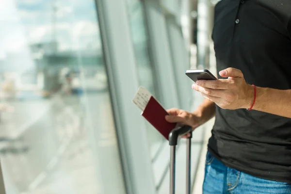 Άνθρωπος εκμετάλλευση κινητό τηλέφωνο, διαβατήρια και επιβίβασης διαβατήριο στο αεροδρόμιο περιμένοντας την πτήση — Φωτογραφία Αρχείου
