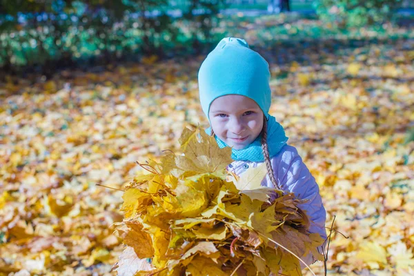 Adorable little girl with yellow maple leaves outdoors at autumn park — Stock Photo, Image
