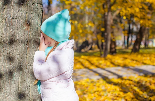 Bambina che gioca a nascondino vicino all'albero nel parco autunnale — Foto Stock