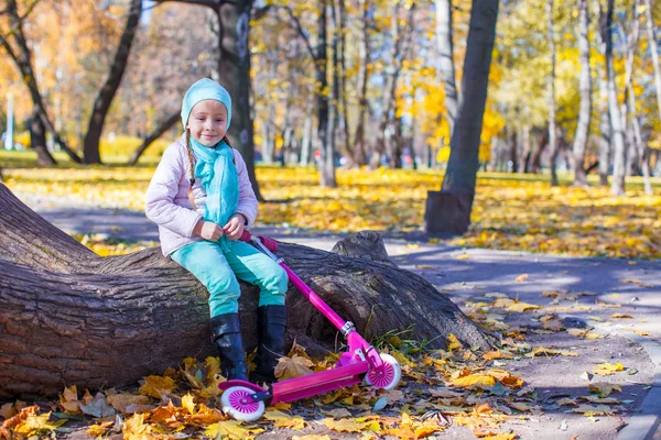 Little cute girl with scooter in the autumn park — Stock Photo, Image