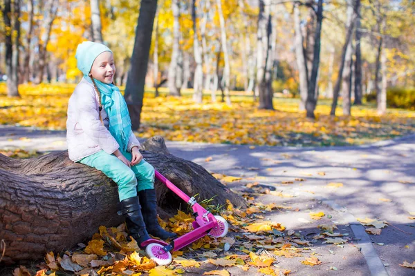 Little happy girl with scooter in the autumn park — Stock Photo, Image