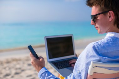 genç işadamı tropik sahilde laptop ve telefon kullanma