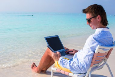 genç işadamı tropik sahilde laptop ve telefon kullanma