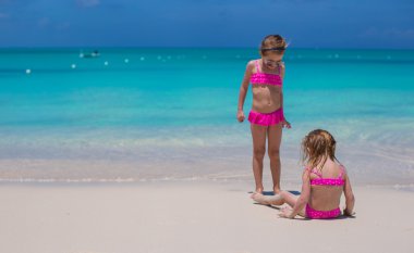 tatil sırasında beyaz kumsalda yürüyen küçük şirin kızlar