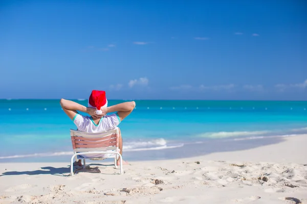 Widok z tyłu młody człowiek w santa hat relaks na plaży krzesło — Zdjęcie stockowe