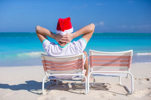 Achteraanzicht van jonge man in christmas hat op strandstoel — Stockfoto