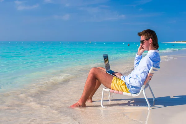 ノート パソコンと熱帯のビーチで携帯電話と若い男 — ストック写真