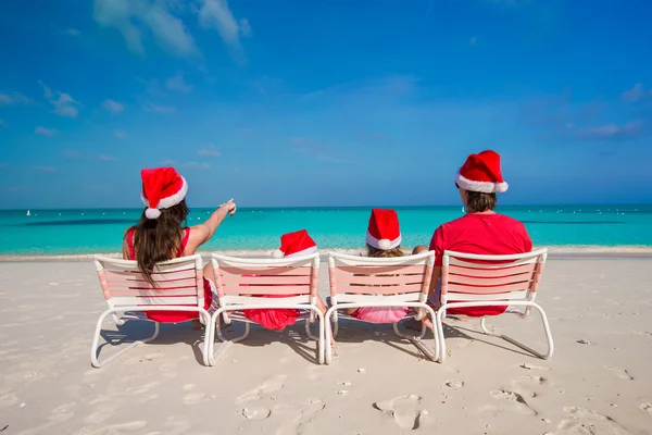 Happy family of four on beach in red Santa hats — Stock Photo, Image