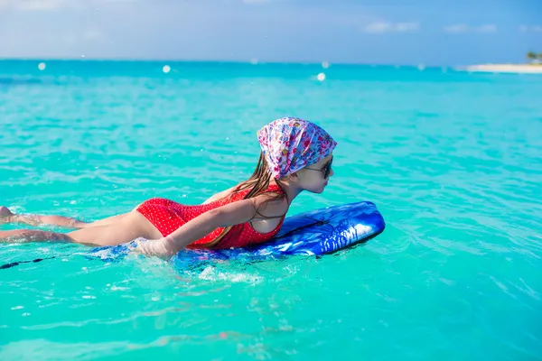 Menina adorável em uma prancha de surf no mar azul-turquesa — Fotografia de Stock