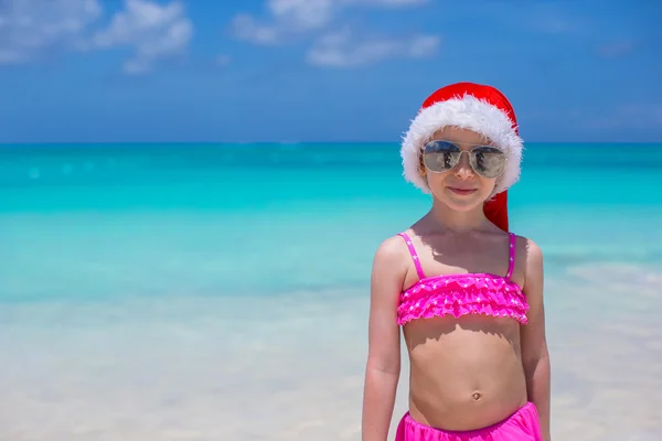 Kleines süßes Mädchen mit rotem Weihnachtsmann-Hut am tropischen Strand — Stockfoto