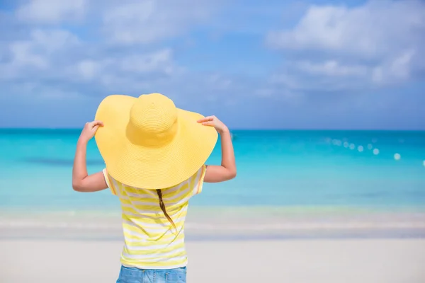 Achteraanzicht van meisje in een grote gele stro hoed op wit zand strand — Stockfoto