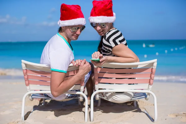 Familie van twee in santa hoeden zittend op het strandstoel — Stockfoto