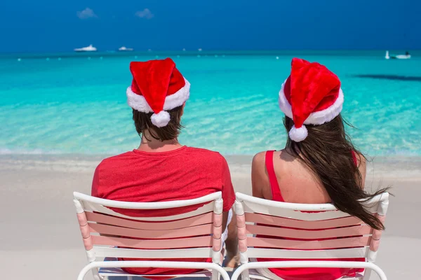 Счастливая молодая пара в красных Санта-Шляпах, сидящая на пляжных стульях — стоковое фото