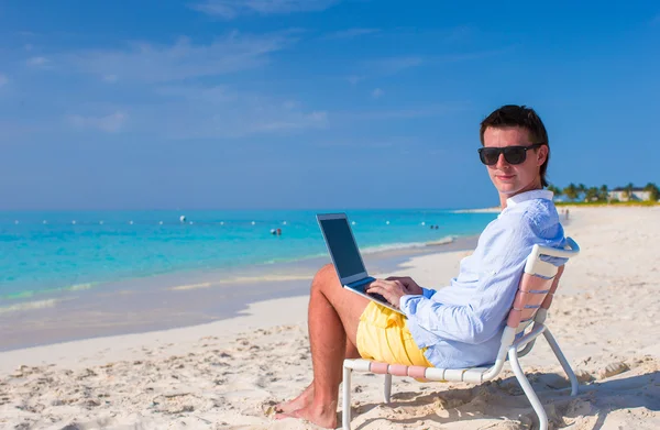 Młody człowiek z laptopa i telefon komórkowy na tropikalnej plaży — Zdjęcie stockowe