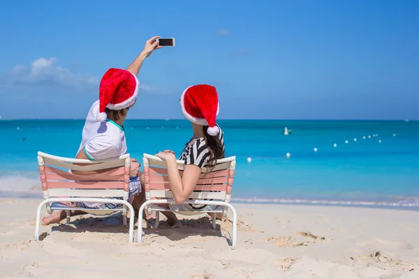Junges glückliches Paar in roten Weihnachtsmützen, das ein Foto mit dem Handy macht — Stockfoto