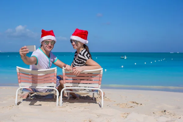 Junges glückliches Paar in roten Weihnachtsmützen, das ein Foto mit dem Handy macht — Stockfoto