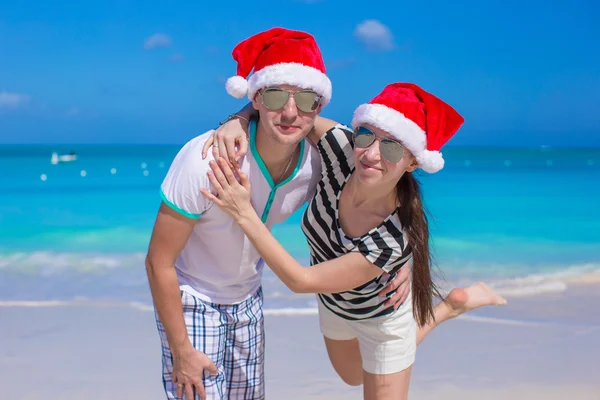 Portret van een jong koppel in santa hoeden genieten van strandvakantie — Stockfoto