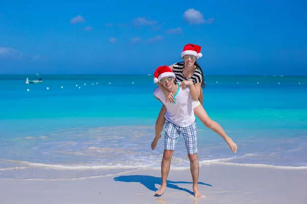 Mladý šťastný pár v červené santa klobouky během jejich tropické dovolené — Stock fotografie