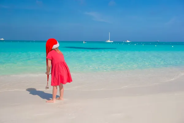 Kleines süßes Mädchen mit rotem Weihnachtsmann-Hut am Strand — Stockfoto