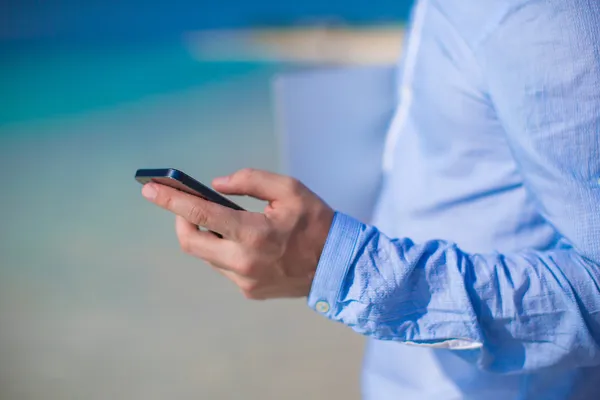 Close-up van telefoon in mannenhand op tropisch strand — Stockfoto