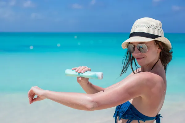 Lächelnde junge Frau trägt Sonnencreme am Strand auf — Stockfoto