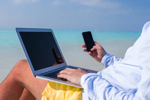 Jonge man die op laptop werkt op tropisch strand — Stockfoto