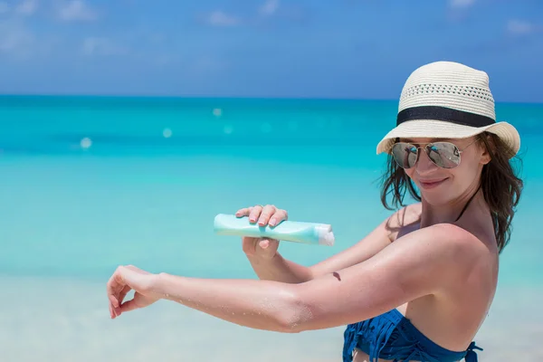 Mujer joven aplicando crema solar en la playa — Foto de Stock