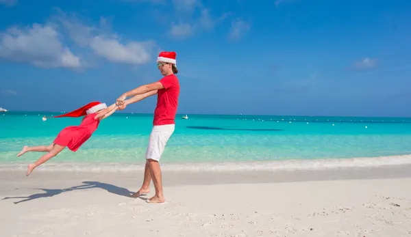小さな女の子と幸せなお父さんサンタ帽子で熱帯のビーチで楽しい時を過す — ストック写真