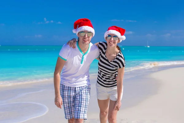 Young happy couple in red Santa hats on tropical beach — Stock Photo, Image