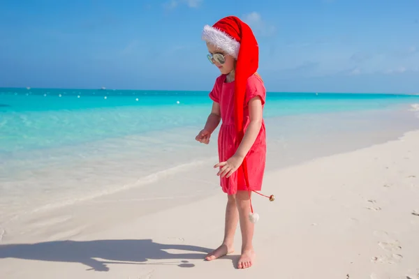 Kleines süßes Mädchen mit rotem Weihnachtsmann-Hut am Strand — Stockfoto