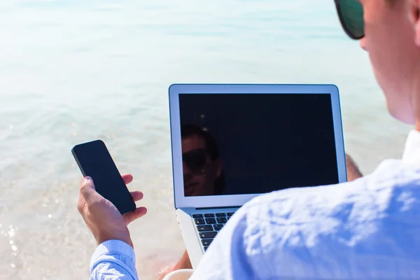 Jonge man die op laptop werkt op tropisch strand — Stockfoto