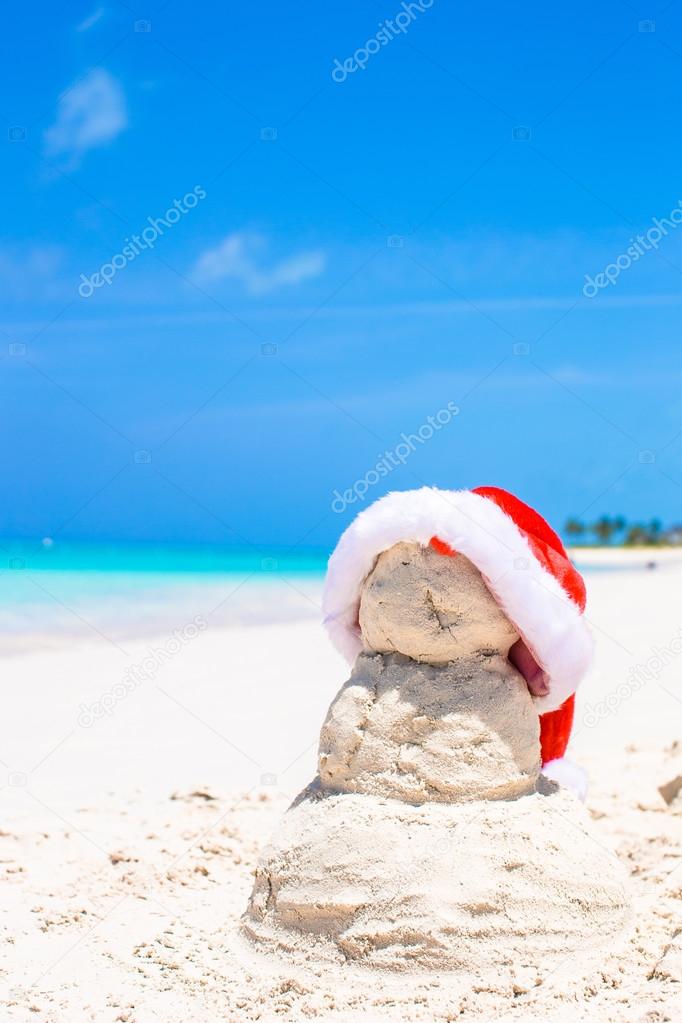 Sandy snowman with red Santa Hat on white Caribbean beach