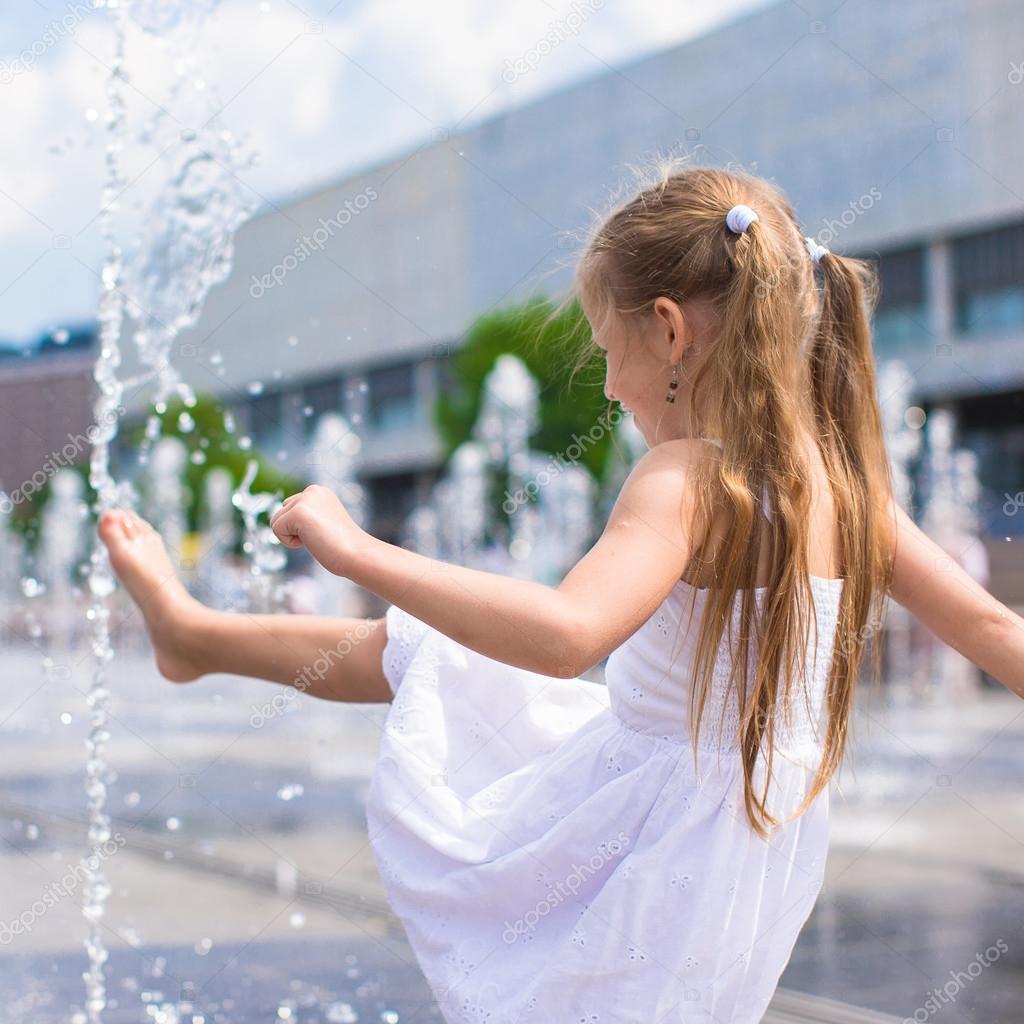 Little girl have fun in open street fountain at hot summer day